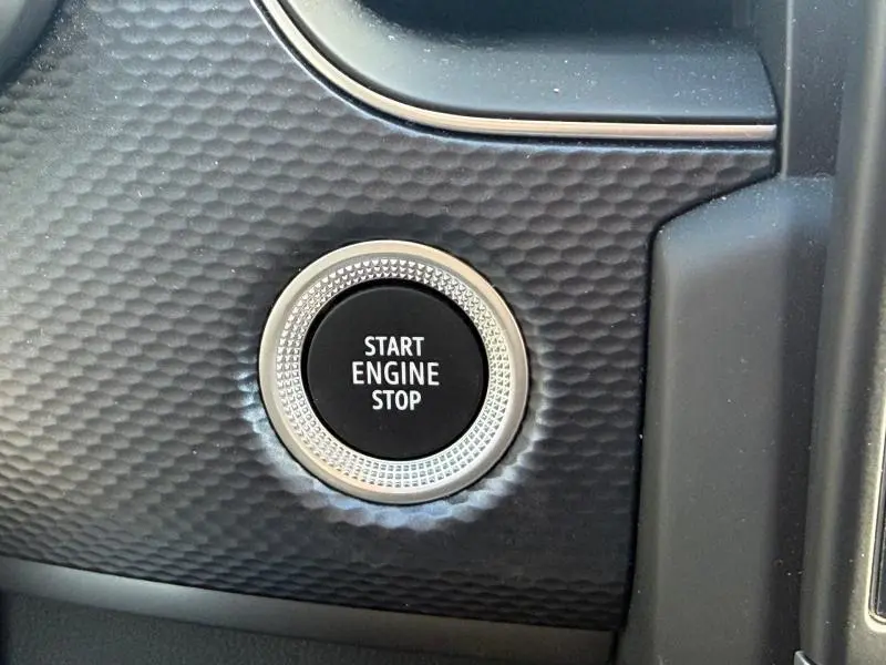 Gros plan sur le bouton Start Engine Stop entouré d’un cerclage argenté, sur le tableau de bord texturé gris métallique du Renault Arkana 2025.