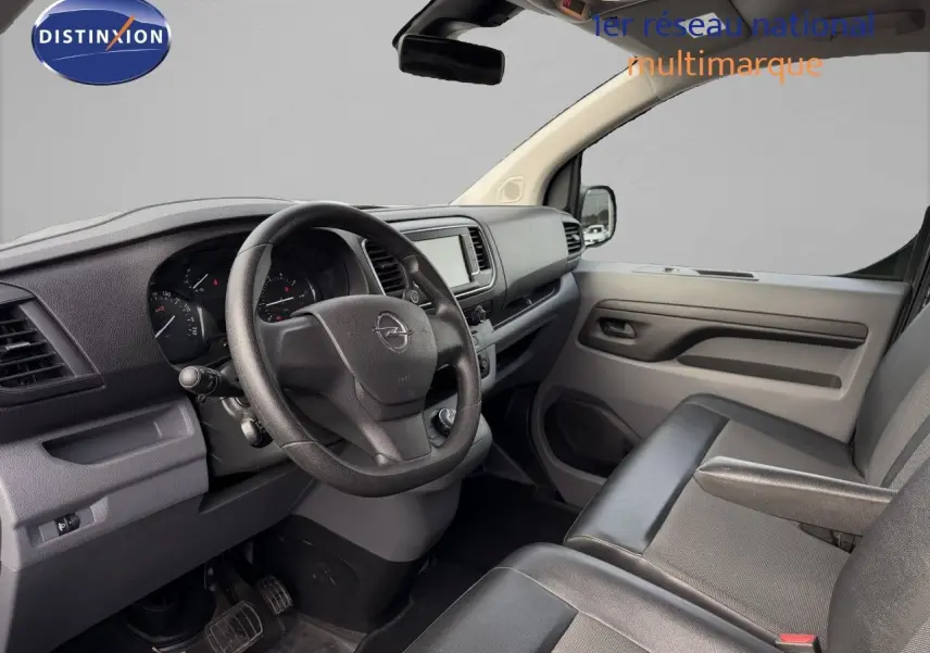 Vue intérieure côté conducteur de l'Opel Vivaro 2020, tableau de bord et sièges en tissu noir visibles.