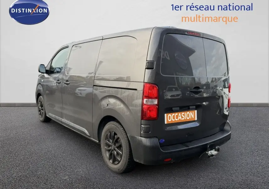 Vue 3/4 arrière droite d’un Opel Vivaro gris titane métal avec attelage et jantes noires, sur fond neutre.