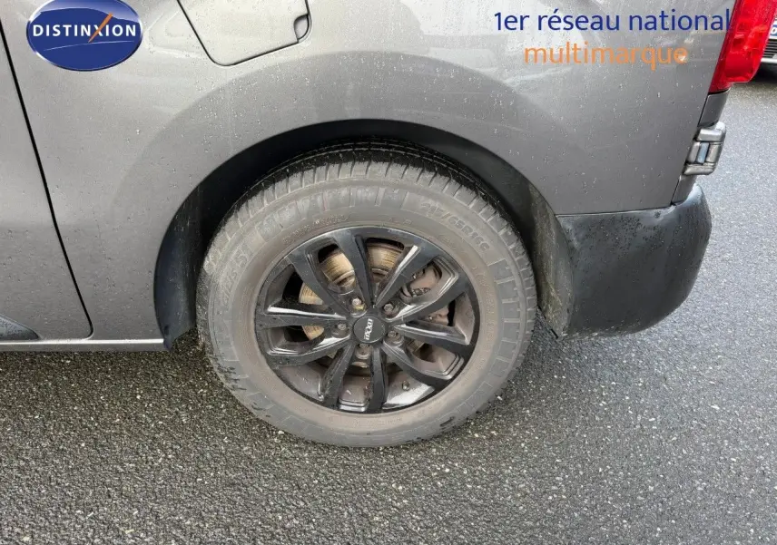 Gros plan sur la roue arrière droite d’un Opel Vivaro gris titane métal avec jante noire et carrosserie mouillée.
