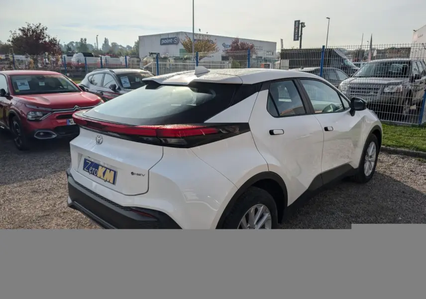 Toyota C-HR blanc vu en 3/4 arrière droit, avec feux arrière full LED et poignées affleurantes noires.