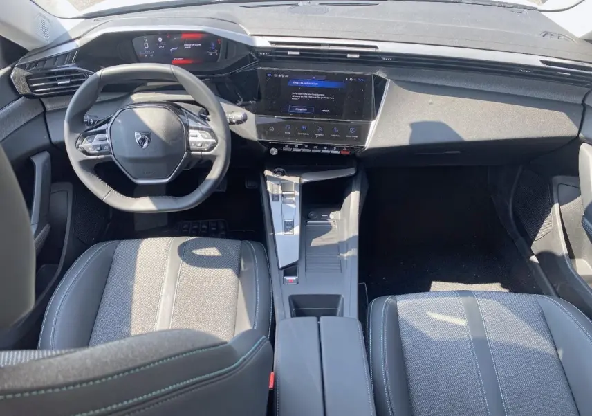 Vue intérieure avant de la Peugeot 308 SW 2025, tableau de bord noir avec écran tactile et volant multifonction.