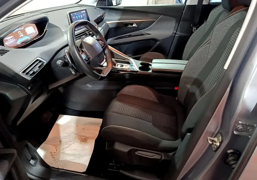 Vue intérieure côté conducteur du Peugeot 5008 gris clair 2020, mettant en valeur le tableau de bord digital et les sièges tissu bicolores.