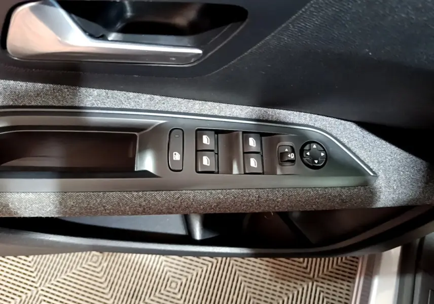 Gros plan sur la commande des vitres et rétroviseurs côté conducteur du Peugeot 5008 gris clair, intérieur tissu gris.