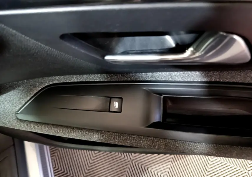 Gros plan sur la poignée intérieure et le bouton de lève-vitre côté conducteur du Peugeot 5008 gris clair 2020.