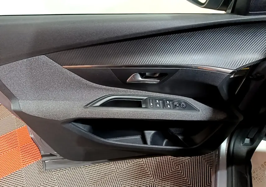 Vue rapprochée de la porte avant gauche du Peugeot 5008 gris clair, montrant les commandes des vitres et le revêtement texturé.