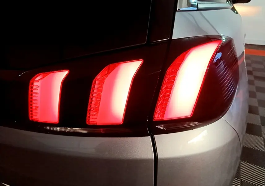 Gros plan sur le feu arrière droit allumé d’un Peugeot 5008 gris clair, vue arrière en intérieur.