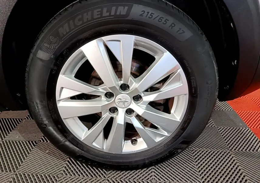 Gros plan sur la roue avant droite d’un Peugeot 5008 gris clair avec jante alliage et pneu Michelin.