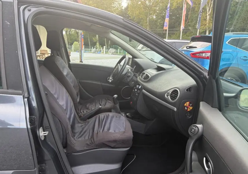 Vue intérieure côté conducteur d'une Renault Clio III gris 2005, montrant les sièges et la console centrale avec boîte manuelle.