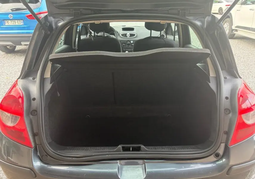 Coffre ouvert d’une Renault Clio III gris 2005, vue arrière montrant l’espace de chargement et l’intérieur des sièges avant.