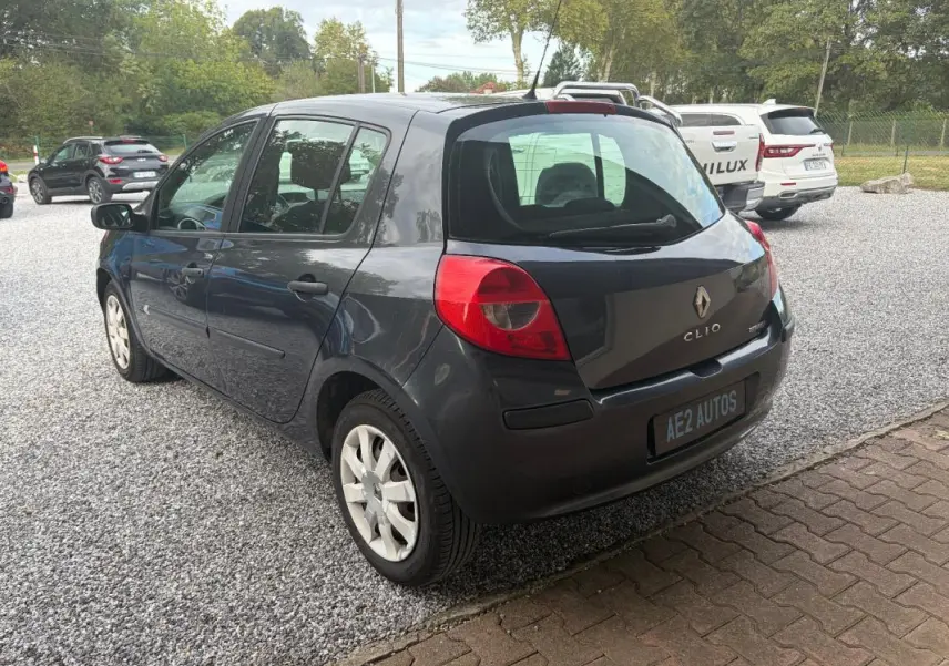 Renault Clio III gris vue 3/4 arrière droit, avec feux arrière rouges et plaque AE2 AUTOS visible.