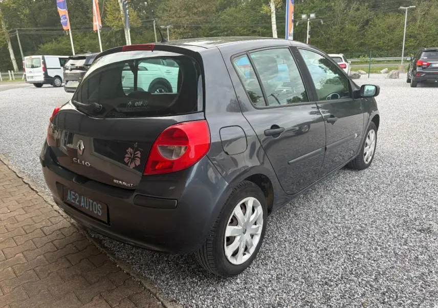 Vue 3/4 arrière droite d'une Renault Clio III gris foncé de 2005 avec jantes acier et feux arrière rouges.
