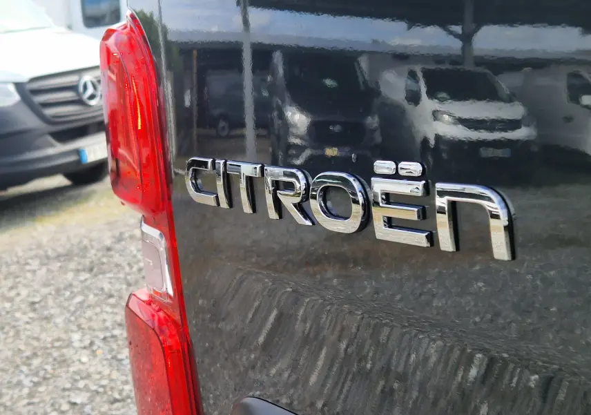 Gros plan sur le logo Citroën à l'arrière d'un utilitaire gris titane, avec feu arrière rouge visible en angle latéral gauche.