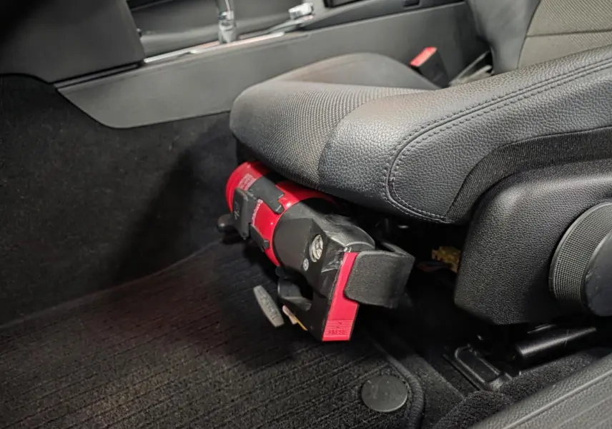 Vue rapprochée sous le siège conducteur d'une Mercedes Classe E Coupé gris, montrant un extincteur rouge fixé au cadre.