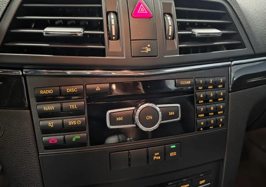 Console centrale noire de la Mercedes Classe E Coupé 2012 avec commandes radio, navigation et climatisation visibles en gros plan