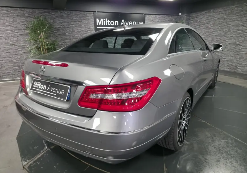 Vue 3/4 arrière droite d'une Mercedes Classe E Coupé gris métallisé avec jantes alliage 19 pouces dans un showroom.