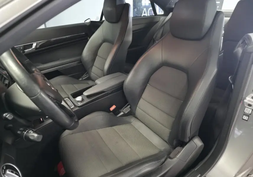 Vue intérieure côté conducteur du coupé Mercedes Classe E 200 gris, sièges en similicuir noir avec accoudoir central.