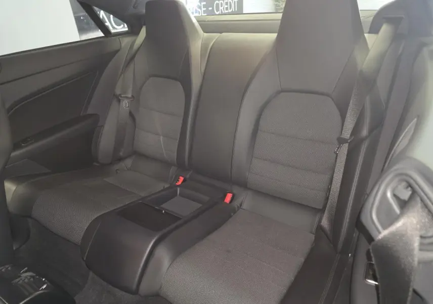 Vue arrière intérieure du coupé Mercedes Classe E 200 gris, montrant les sièges arrière en tissu et similicuir noir avec accoudoir central.