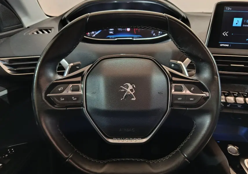 Vue rapprochée du volant cuir noir de la Peugeot 3008 avec commandes intégrées et tableau de bord numérique.
