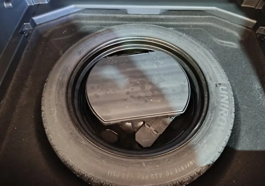 Vue rapprochée de la roue de secours noire dans le coffre d'un Peugeot 3008 blanc, entourée de moquette noire.