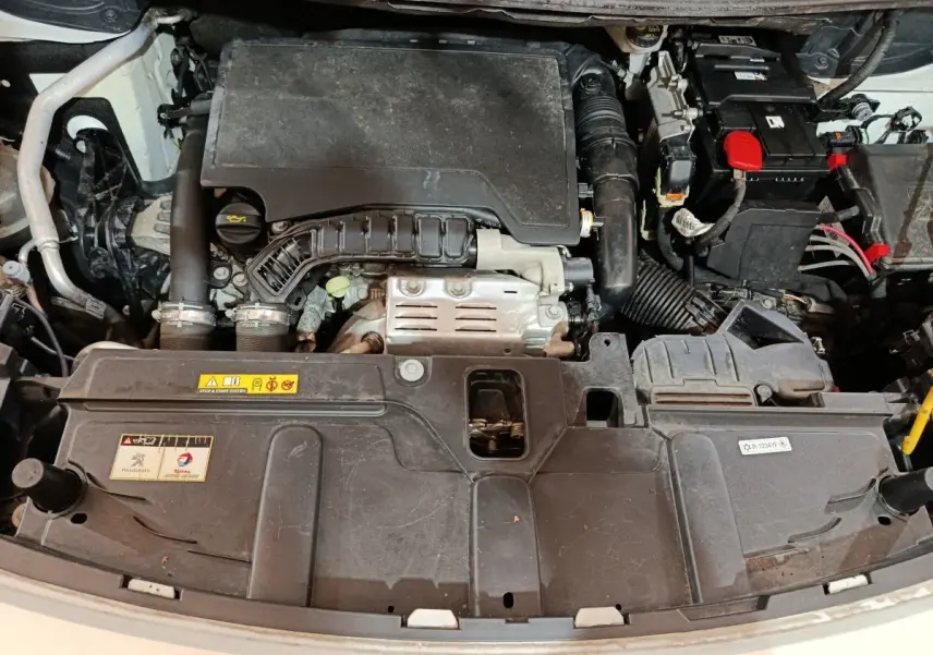 Vue plongeante sur le moteur essence d’un Peugeot 3008 blanc, version Puretech 130 avec capot ouvert.