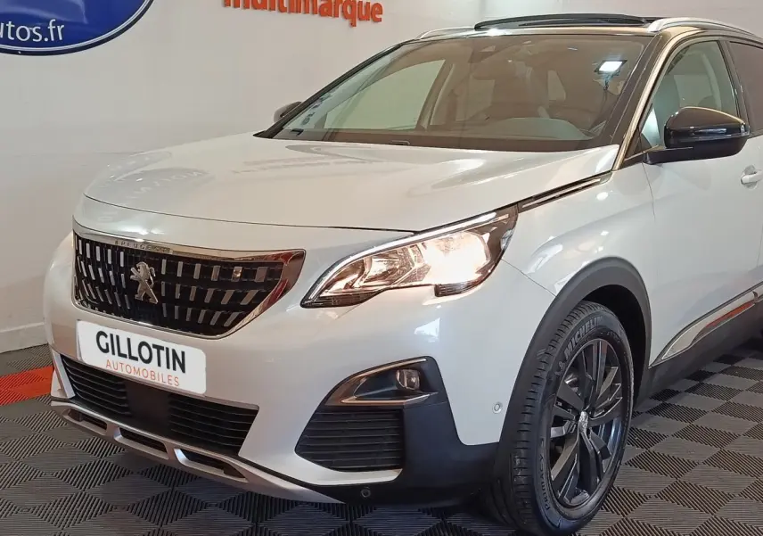 Vue 3/4 avant droit d'un Peugeot 3008 blanc avec calandre noire et phares allumés en intérieur showroom.
