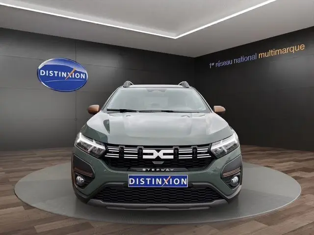 Vue frontale d'une Dacia Sandero Stepway 2025 kaki lichen avec calandre noire et logo distinctif, en showroom.