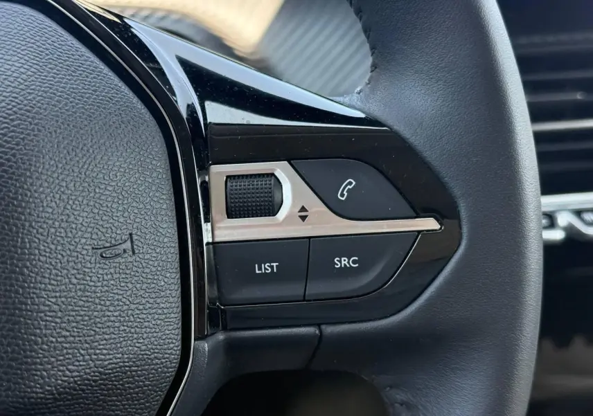 Gros plan sur les commandes audio au volant noir de la Peugeot 208 1.2 100ch Allure 2025.