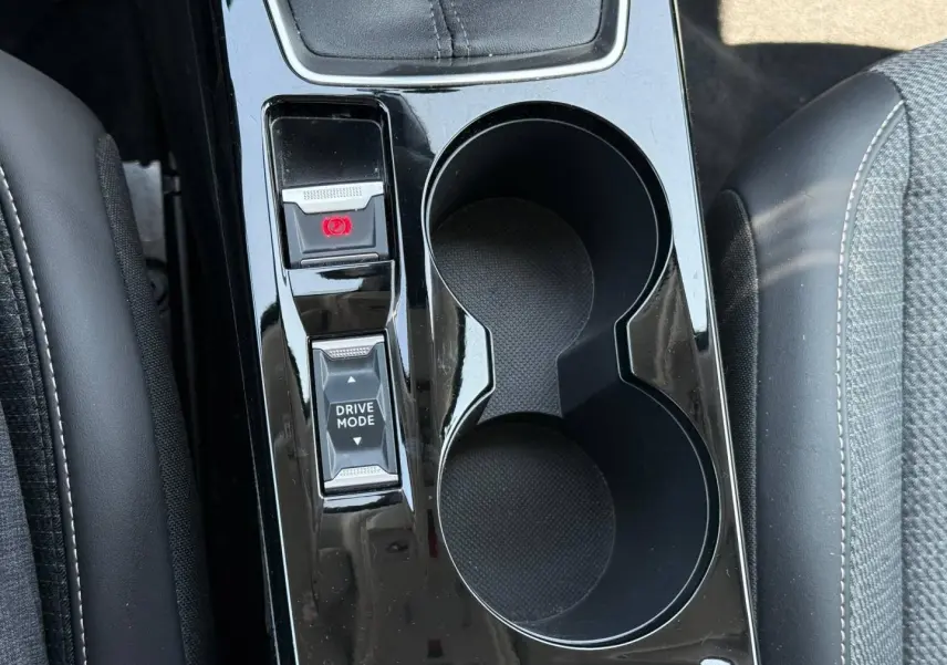 Vue plongeante sur la console centrale noire brillante de la Peugeot 208 gris Artense avec boutons frein à main et mode de conduite.