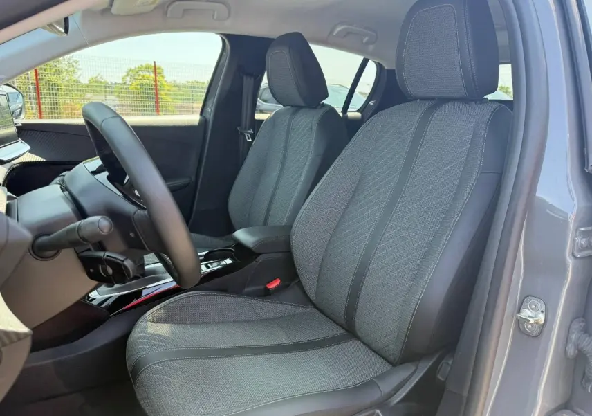 Vue intérieure côté conducteur de la Peugeot 208 1.2 100ch Allure gris Artense, sièges tissu gris avec accoudoir central.