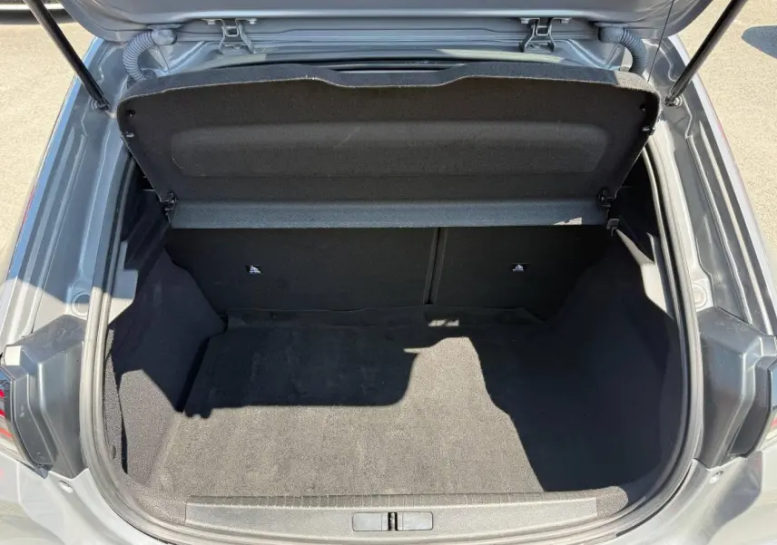 Coffre ouvert vu de dessus d'une Peugeot 208 gris Artense avec intérieur de coffre noir et banquette arrière rabattable.