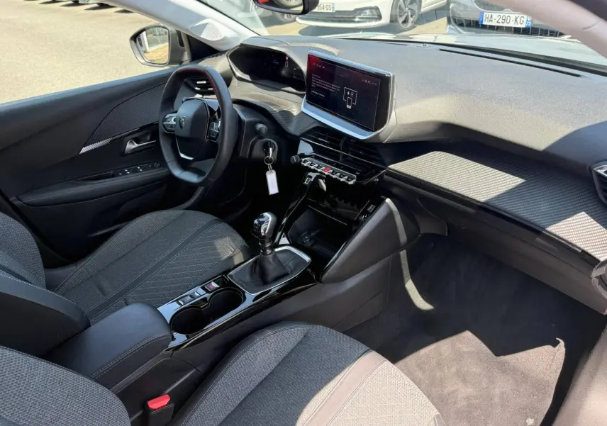 Vue intérieure côté conducteur de la Peugeot 208 1.2 100ch Allure avec tableau de bord moderne et sellerie tissu gris.