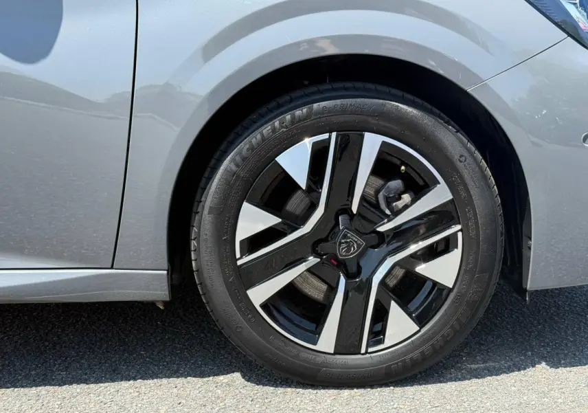 Gros plan sur la roue avant droite d'une Peugeot 208 gris Artense avec jante alu bicolore noire et argent.