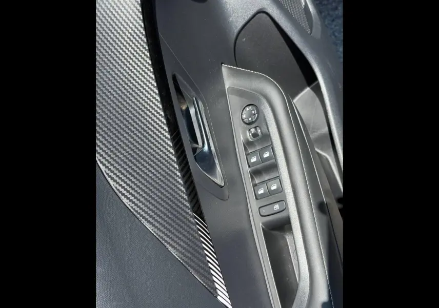 Gros plan sur la porte avant gauche de la Peugeot 208 gris Artense, avec commandes électriques et insert effet carbone.
