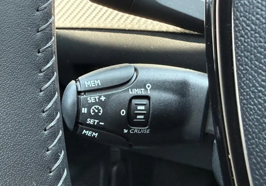 Gros plan sur la commande du régulateur de vitesse au volant d’une Peugeot 208 gris Artense, intérieur noir.
