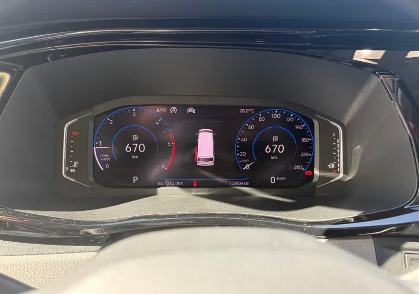 Vue rapprochée du tableau de bord numérique du Volkswagen Transporter blanc, affichant 670 km d'autonomie et 28°C.