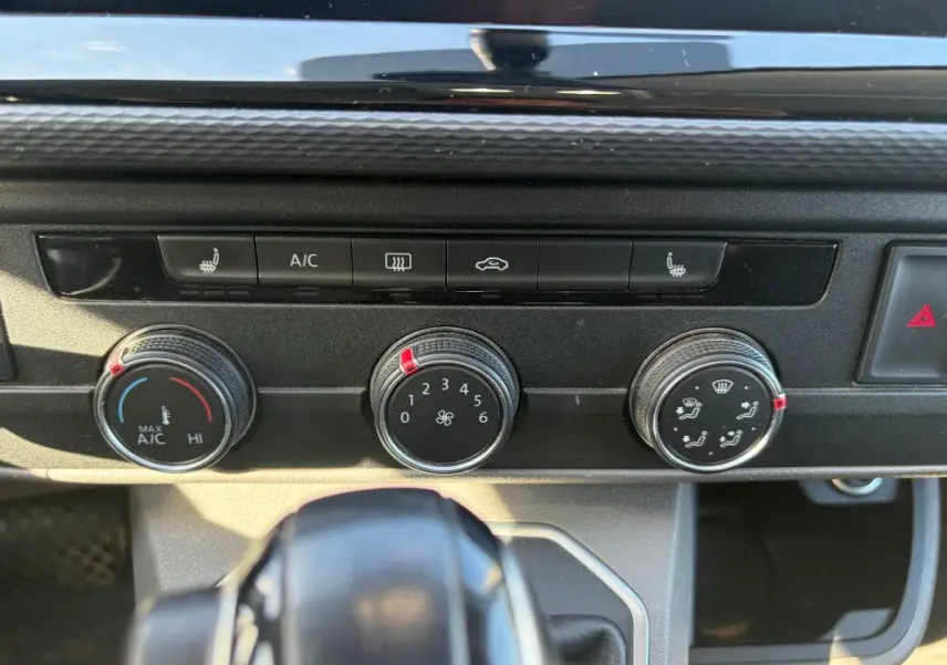 Gros plan sur les commandes de climatisation et ventilation du Volkswagen Transporter blanc, avec boutons rotatifs et indicateurs rouges.