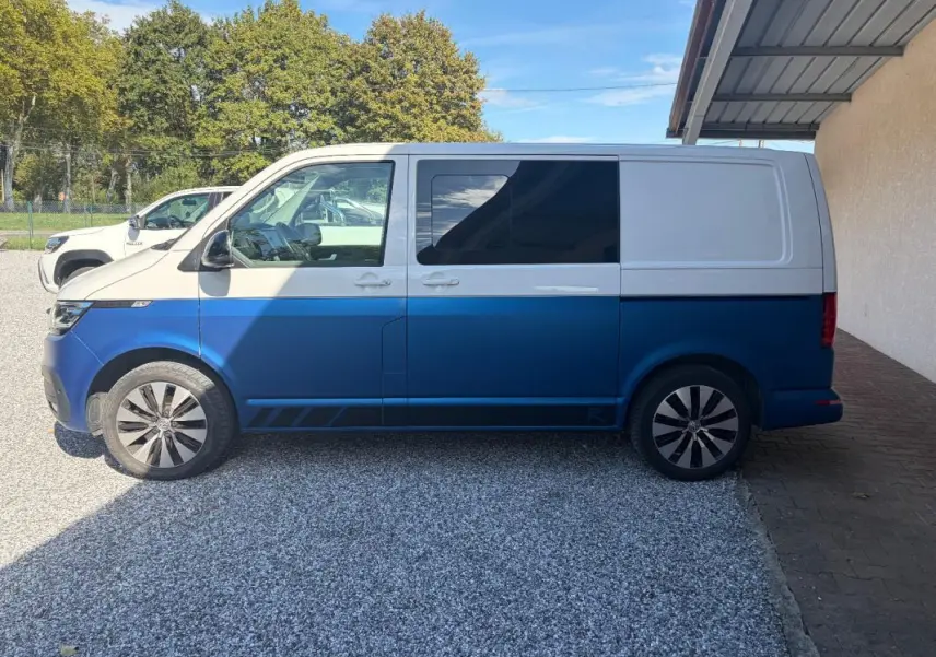 Vue de profil côté gauche d’un Volkswagen Transporter 2.0 TDI blanc et bleu, avec jantes aluminium et vitres teintées.
