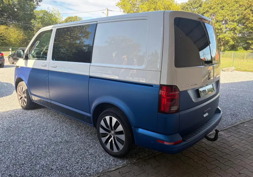 Vue 3/4 arrière droit d'un Volkswagen Transporter 2 tons blanc et bleu avec jantes aluminium et vitres teintées.