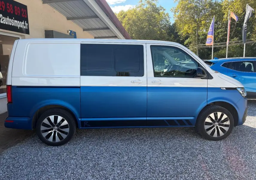 Vue de profil droit d’un Volkswagen Transporter bicolore blanc et bleu, avec jantes aluminium et vitres teintées.
