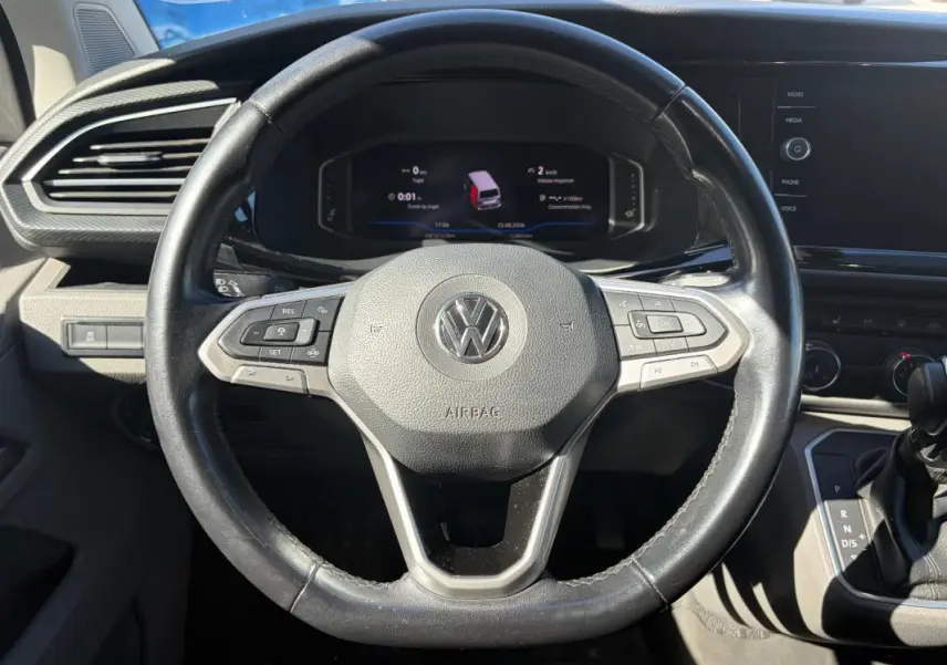 Vue rapprochée du volant cuir noir de Volkswagen Transporter 2020 avec commandes multifonctions et tableau de bord digital.