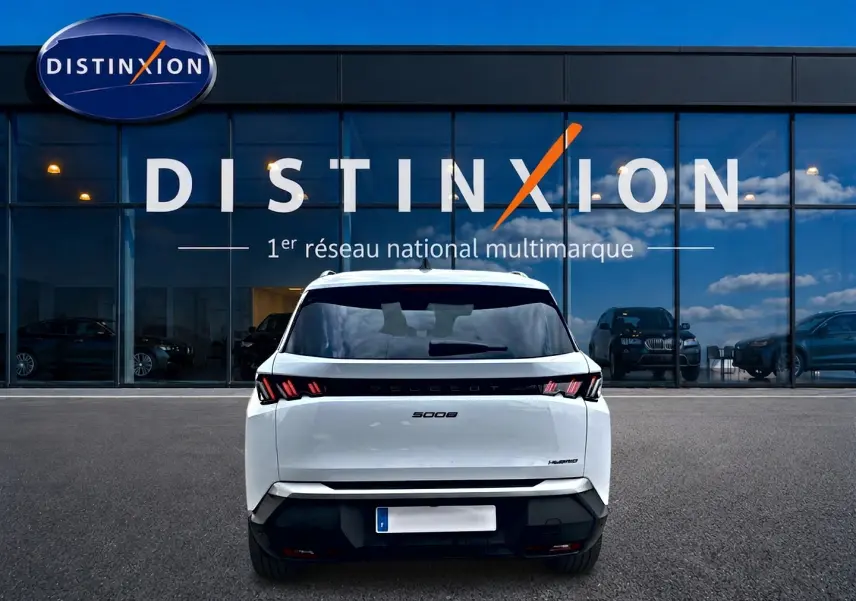 Vue arrière d’un Peugeot 5008 Hybrid blanc garé devant une vitrine avec logo Distinxion.