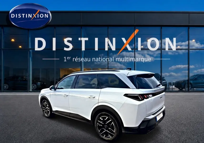 Peugeot 5008 blanc en 3/4 arrière droit, avec jantes alu noires et vitres arrière surteintées devant showroom Distinxion.