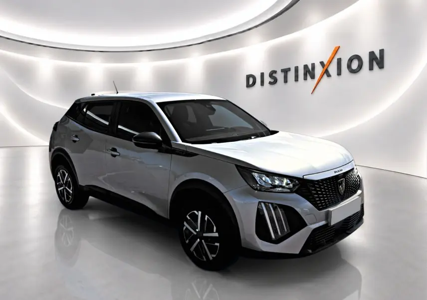 Peugeot 2008 gris en 3/4 avant droit, avec calandre noire et feux LED distinctifs dans un showroom lumineux.