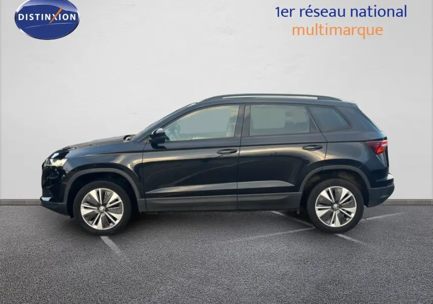 Profil côté gauche d'un Škoda Karoq noir Magic Metal 2023 garé devant un mur blanc, roues alliage bicolore visibles.