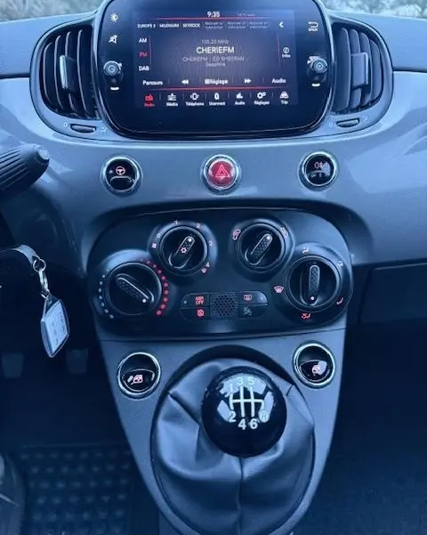 Vue rapprochée du tableau de bord et levier de vitesse manuel de la FIAT 500 Hybrid gris foncé avec écran tactile central allumé.