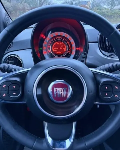 Vue rapprochée du volant noir FIAT avec tableau de bord central éclairé en rouge dans une FIAT 500 Hybrid 2022.