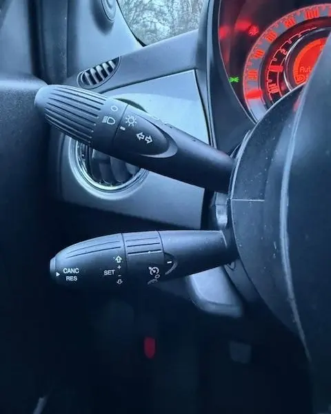 Gros plan sur les commandes au volant de la FIAT 500 Hybrid gris foncé, avec tableau de bord rouge en arrière-plan.