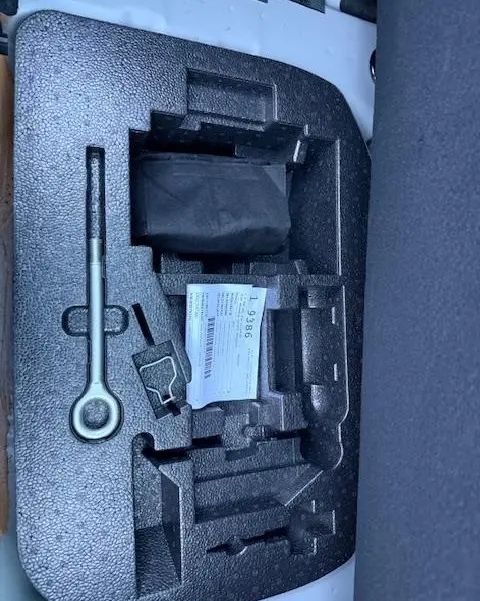 Gros plan sur le rangement en mousse noir dans le coffre d'une FIAT 500 gris foncé, avec outils et notice visibles.
