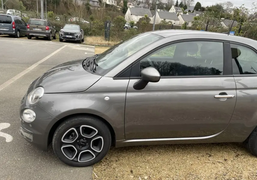 Vue de profil côté gauche d'une FIAT 500 Hybrid gris foncé avec jantes noires et détails chromés sur la poignée.